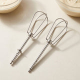 Two stainless steel electric hand mixer beaters placed on a light beige surface, with partial bowls of cream visible in the top corners.