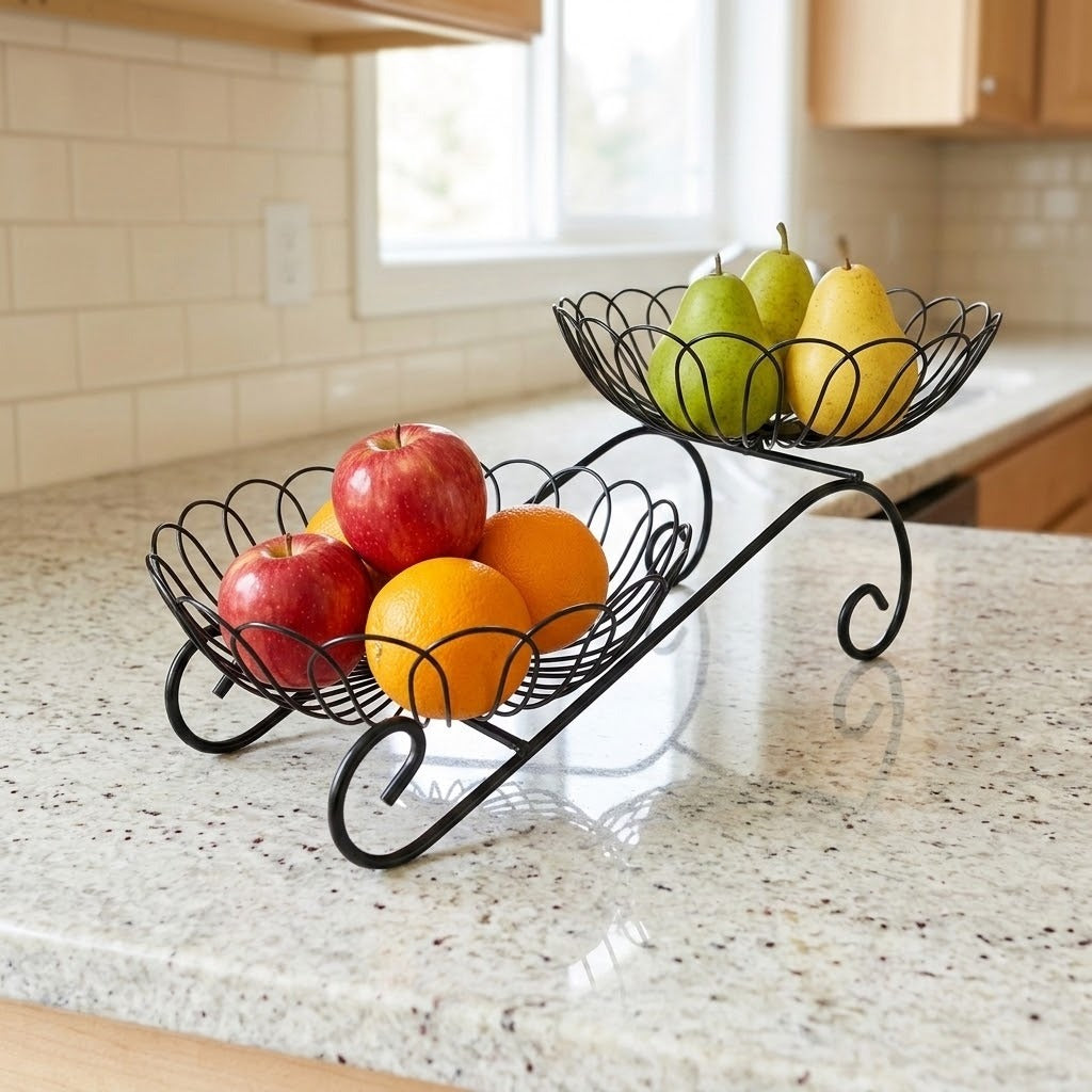 A black metal two-tier fruit basket with scrollwork legs, filled with red apples, oranges, and green and yellow pears, set on a speckled kitchen countertop.