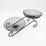 Black metal two-tier wire fruit basket with decorative scrollwork and scalloped bowl edges, shown on a plain white background.