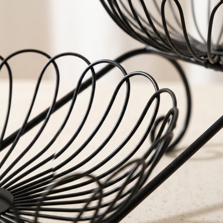 Close-up of a black metal wire spiral rack or basket on a light beige countertop, with part of a matching rack visible in the upper right.