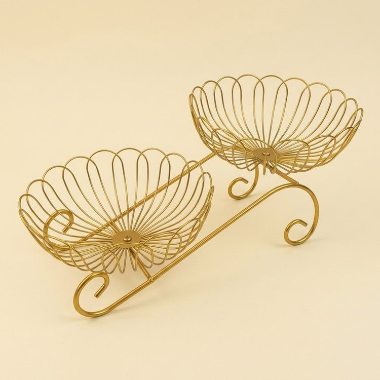 A gold-finished metal wire double-tiered stand with a decorative scroll base, photographed on a solid light beige background.