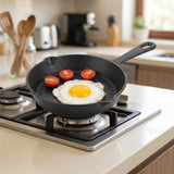 A black cast iron skillet sits on a gas stovetop in a bright kitchen, cooking a sunny-side-up egg with three halved cherry tomatoes.