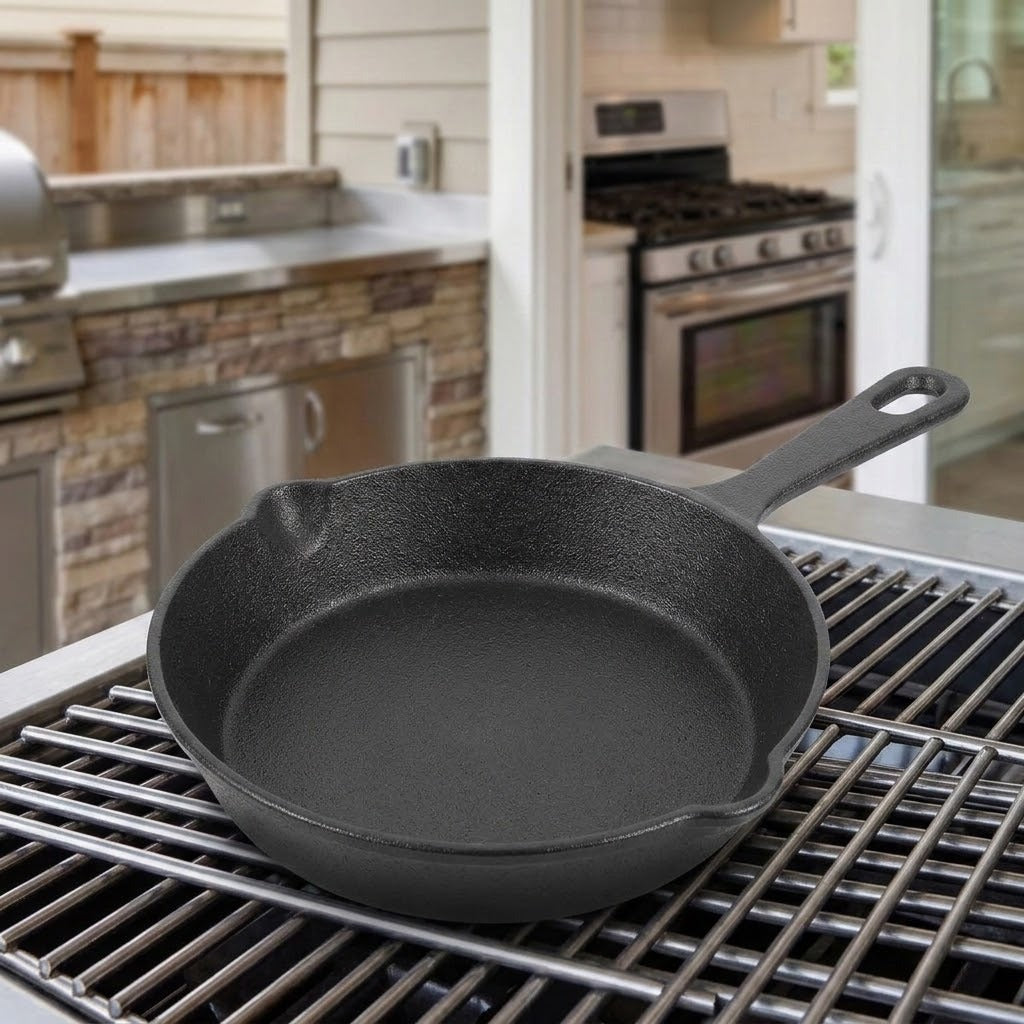 A black cast iron skillet sits on a metal grill grate in a kitchen setting, with a stove and stone-tile backsplash visible in the background.