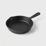 A classic black cast iron skillet with a single loop handle, photographed on a clean, light gray studio background.