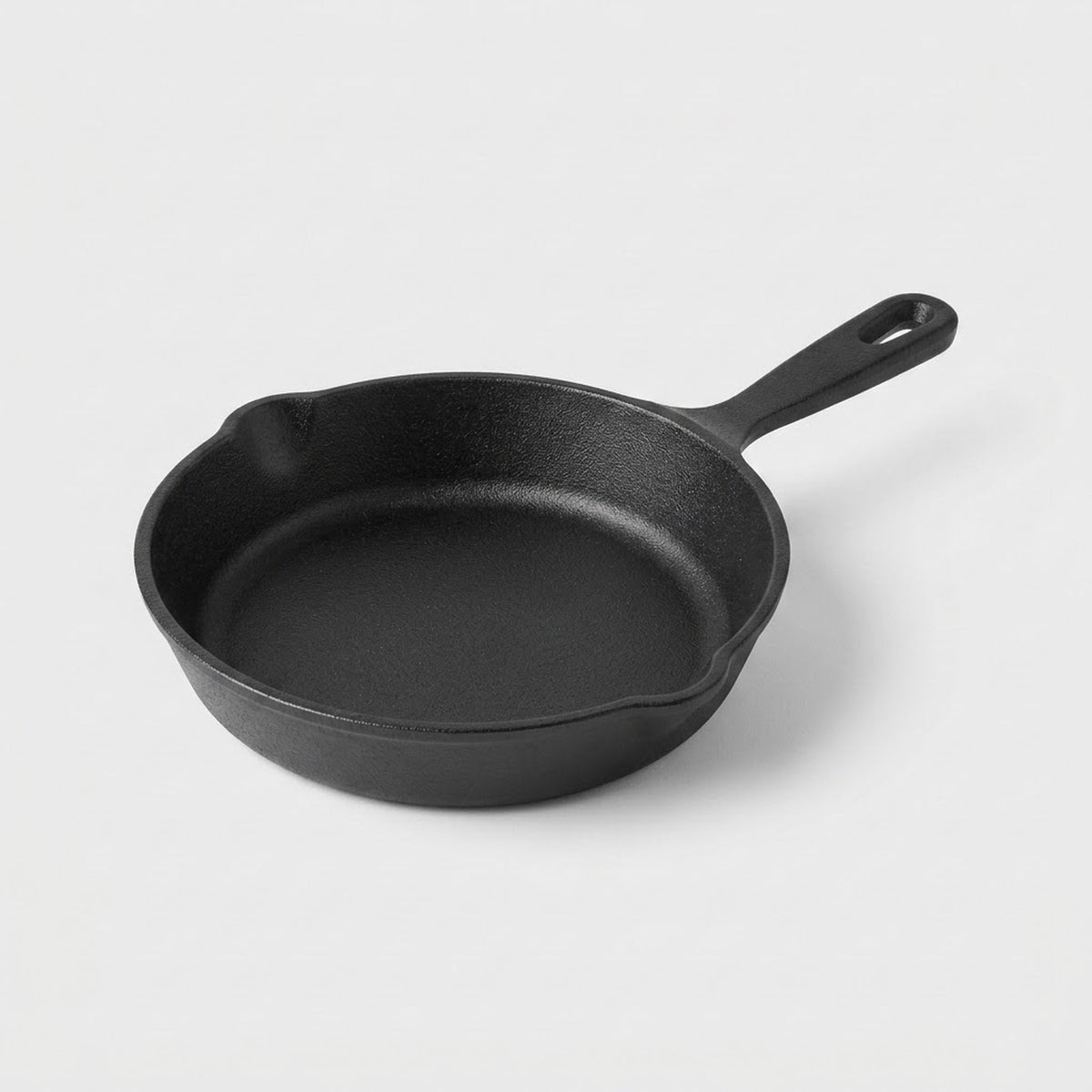 A classic black cast iron skillet with a single loop handle, photographed on a clean, light gray studio background.
