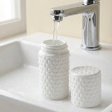Two white textured mason-jar-style containers with a honeycomb pattern sit in a white sink under a chrome faucet, with water flowing into the larger container.