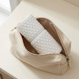 A beige canvas zip pouch with a honeycomb-textured white insert, shown open on a light cream tabletop.