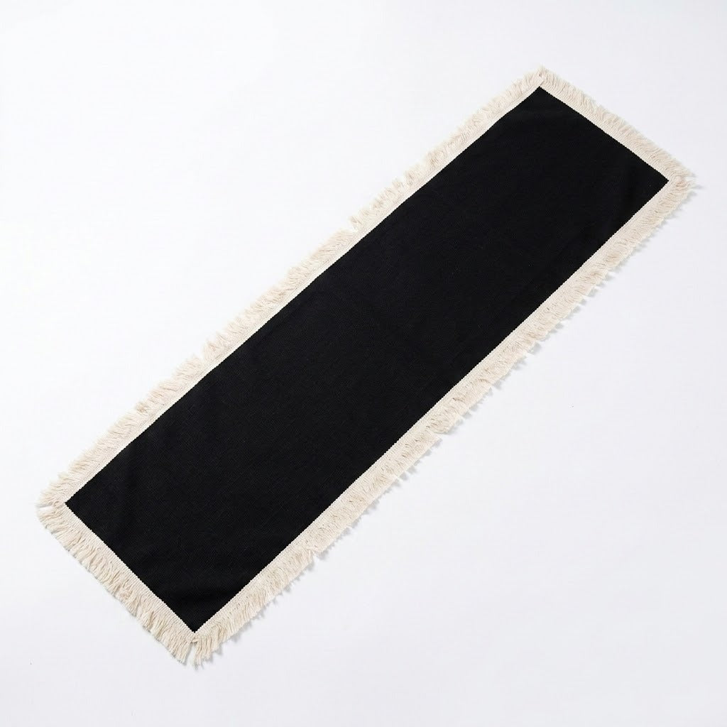 A long rectangular black runner with cream fringe on all sides, photographed on a plain white background.