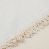 Close-up of a cream-colored woven textile with a fringed edge, shown against a matching light neutral background.
