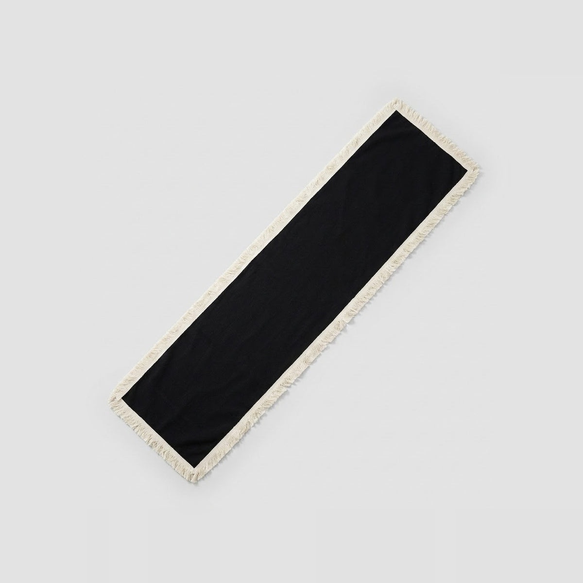 A long rectangular black scarf with a cream-colored fringed border, shown diagonally on a light gray background.