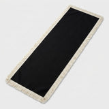 A rectangular black runner rug with cream-colored fringe on all sides, photographed on a light gray background.