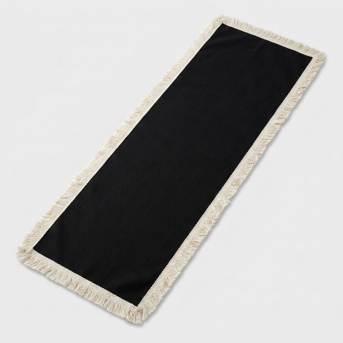 A rectangular black runner rug with cream-colored fringe on all sides, photographed on a light gray background.