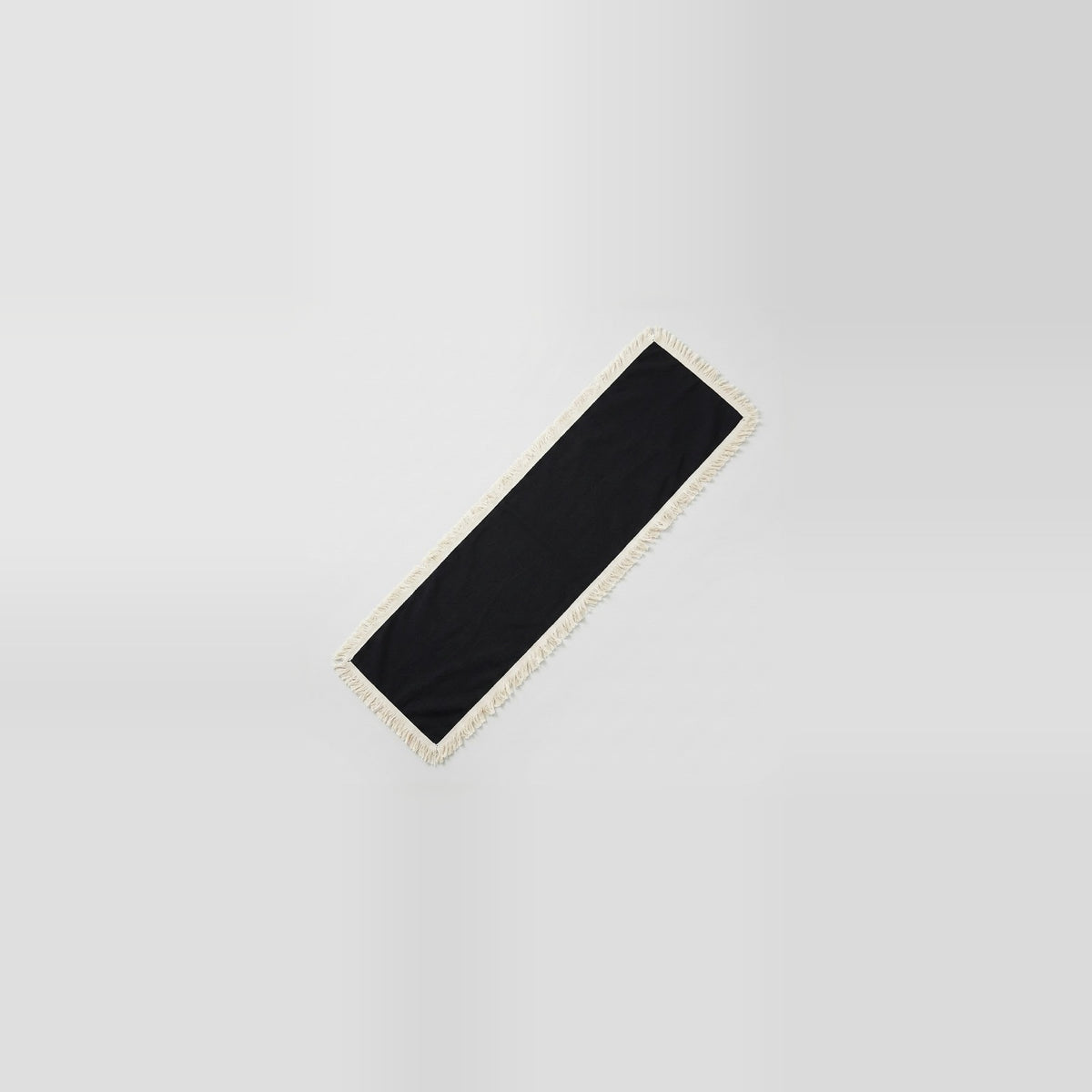 A long, narrow black rectangular mat or runner with a light beige fringed edge, shown diagonally on a light gray gradient background.