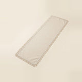 A long rectangular fringed textile runner in a warm off-white or cream tone, photographed on a plain light beige background.