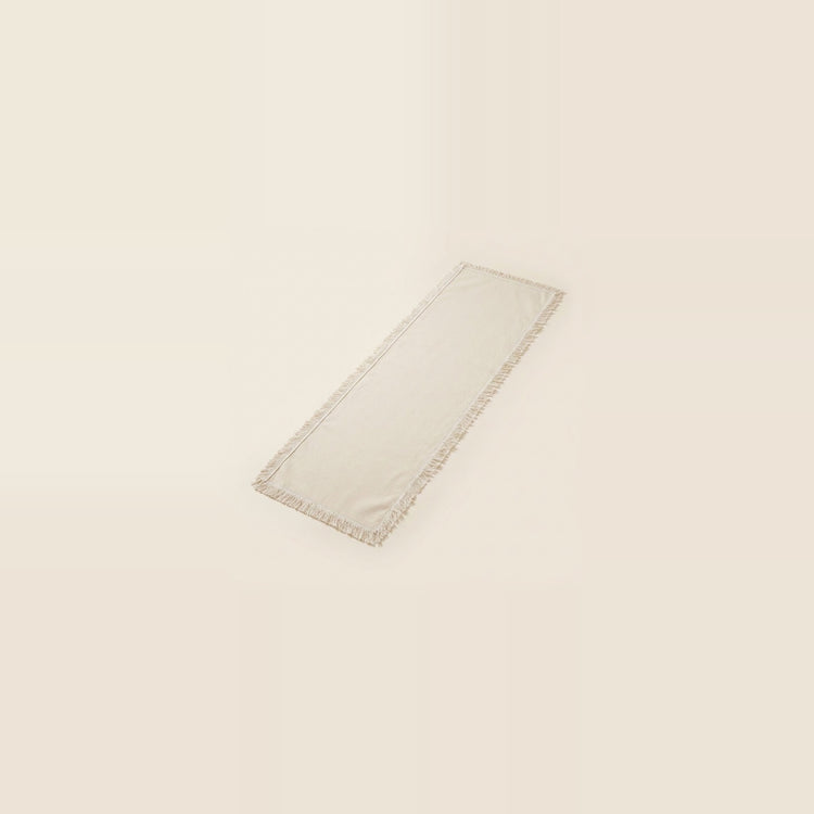 A long rectangular cream-colored fabric runner with a delicate fringed edge, shown on a solid cream background.