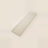 A long rectangular cream-colored table runner with fringed edges, shown on a solid light beige background.