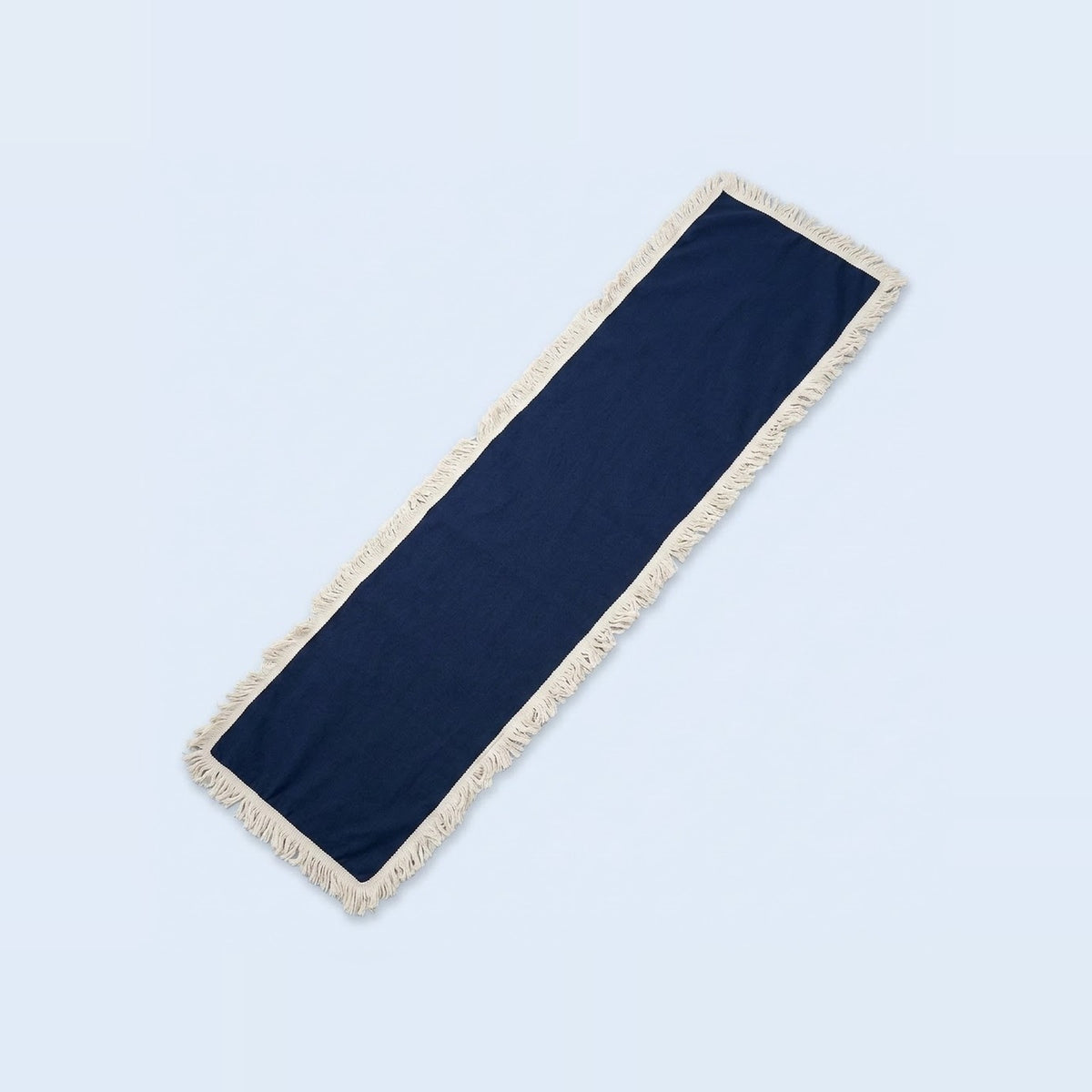 A long rectangular navy blue fabric runner with cream fringe trim on all sides, shown diagonally on a light blue background.