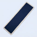 A long rectangular navy blue runner rug with cream-colored fringe on all sides, shown diagonally on a light blue background.
