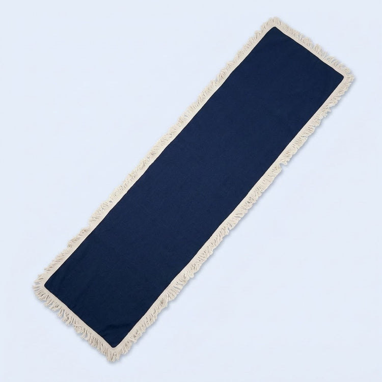 A long rectangular navy blue runner rug with cream-colored fringe on all sides, shown diagonally on a light blue background.