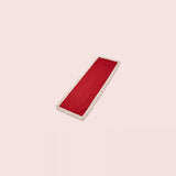 A long rectangular red runner with white fringe trim on both ends, displayed diagonally on a solid pale pink background.