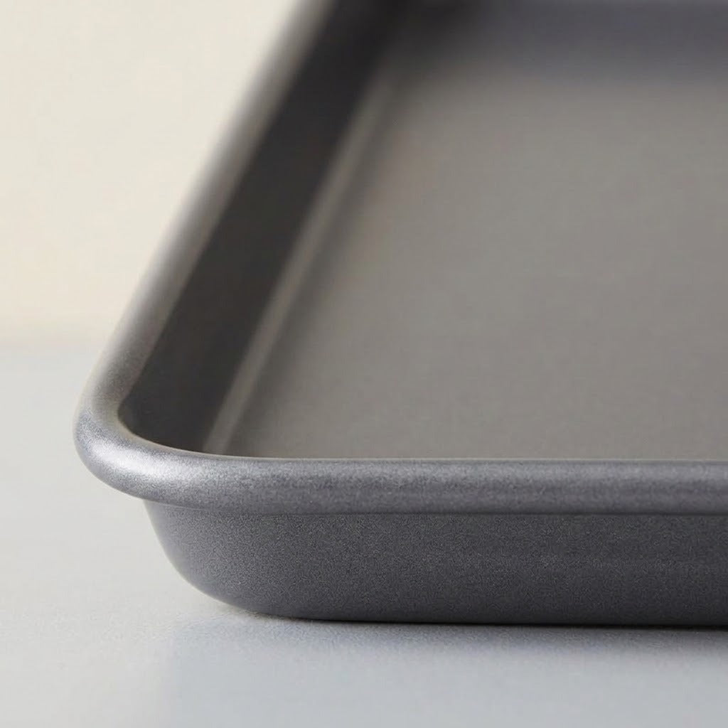 Close-up of a dark gray metal baking pan showing the corner and rim detail against a light neutral background.