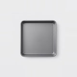 A square gray metal baking pan with raised rounded corners, shown from a top-down view on a clean white background.