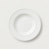 A white ceramic plate with a decorative beaded border, photographed from directly above on a clean, light off-white background.