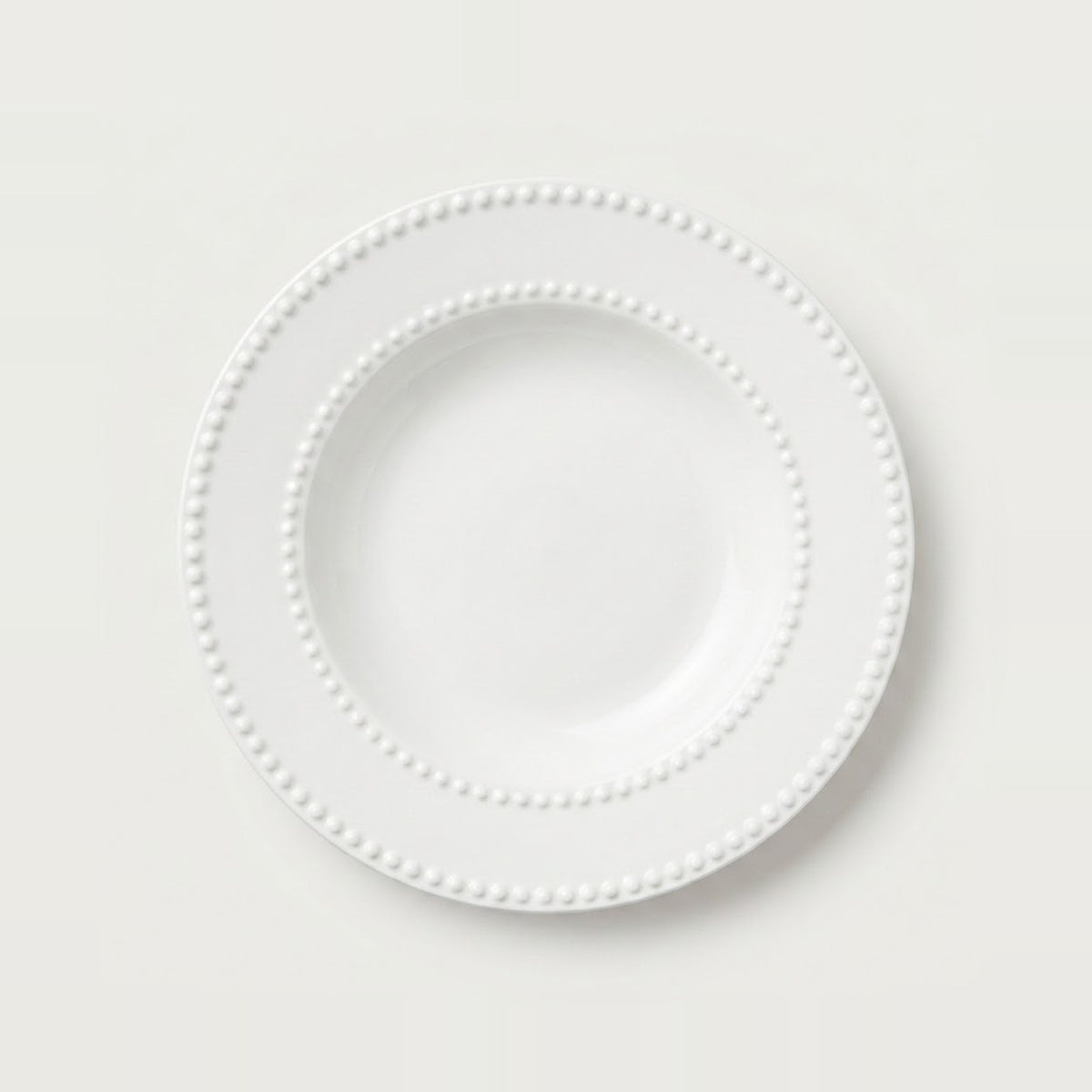 A white ceramic plate with a decorative beaded border, photographed from directly above on a clean, light off-white background.