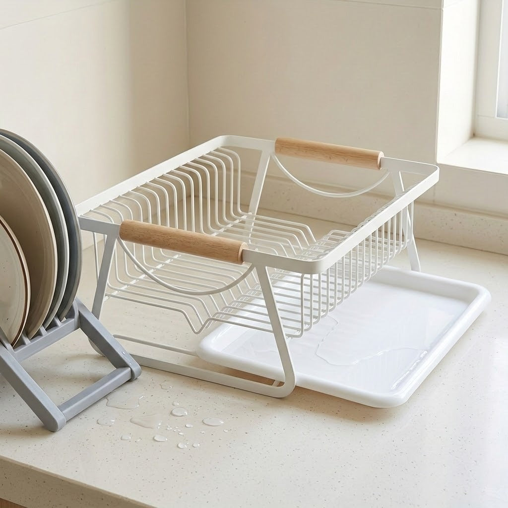 A white wire kitchen dish rack with light wood handles and a white tray, shown on a kitchen counter next to stacked plates.