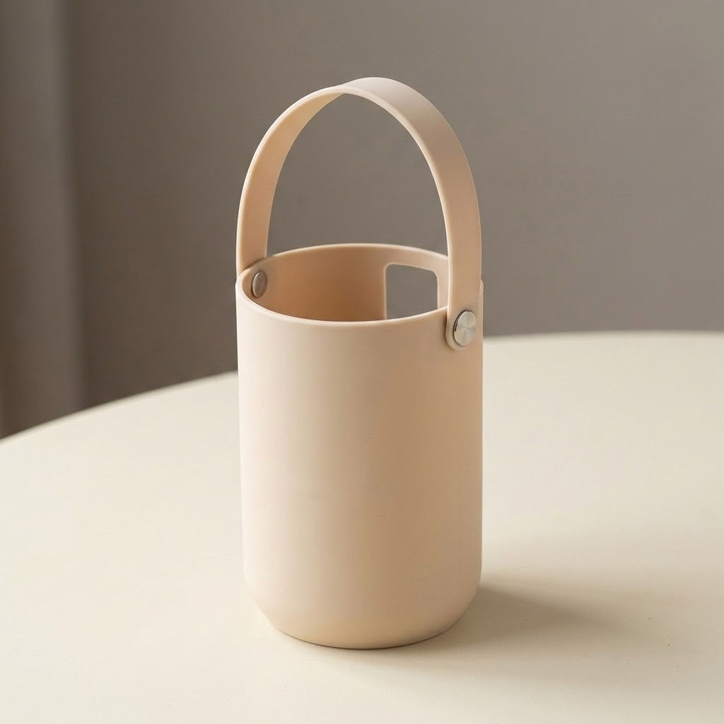 A minimalist, matte beige cylindrical container with a matching arched handle, resting on a light cream-colored table against a soft gray background.