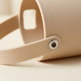 Close-up of a beige plastic container with a matching handle and a silver metal rivet, resting on a textured beige surface.