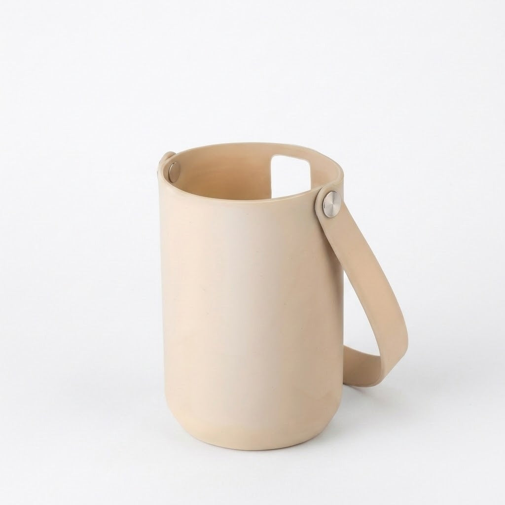 A minimalist light beige leather cylindrical cup with a matching leather handle and a small metal rivet, shown on a seamless white background.