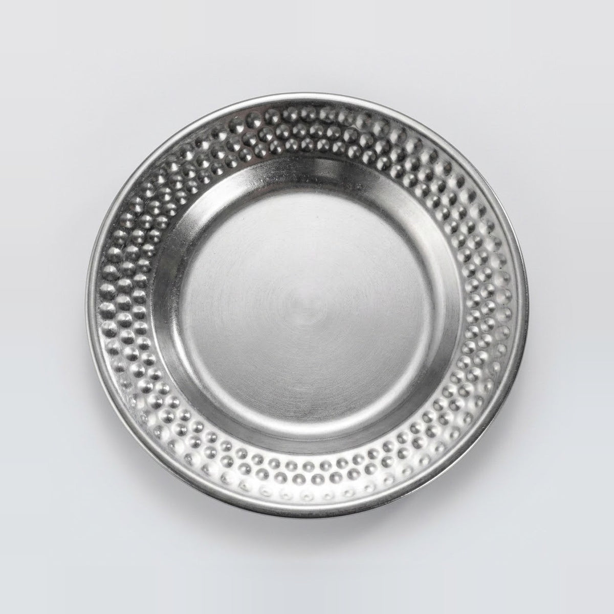 A round silver metal plate with a textured, dimpled border and a smooth, reflective center, shown from a top-down perspective on a light gray background.