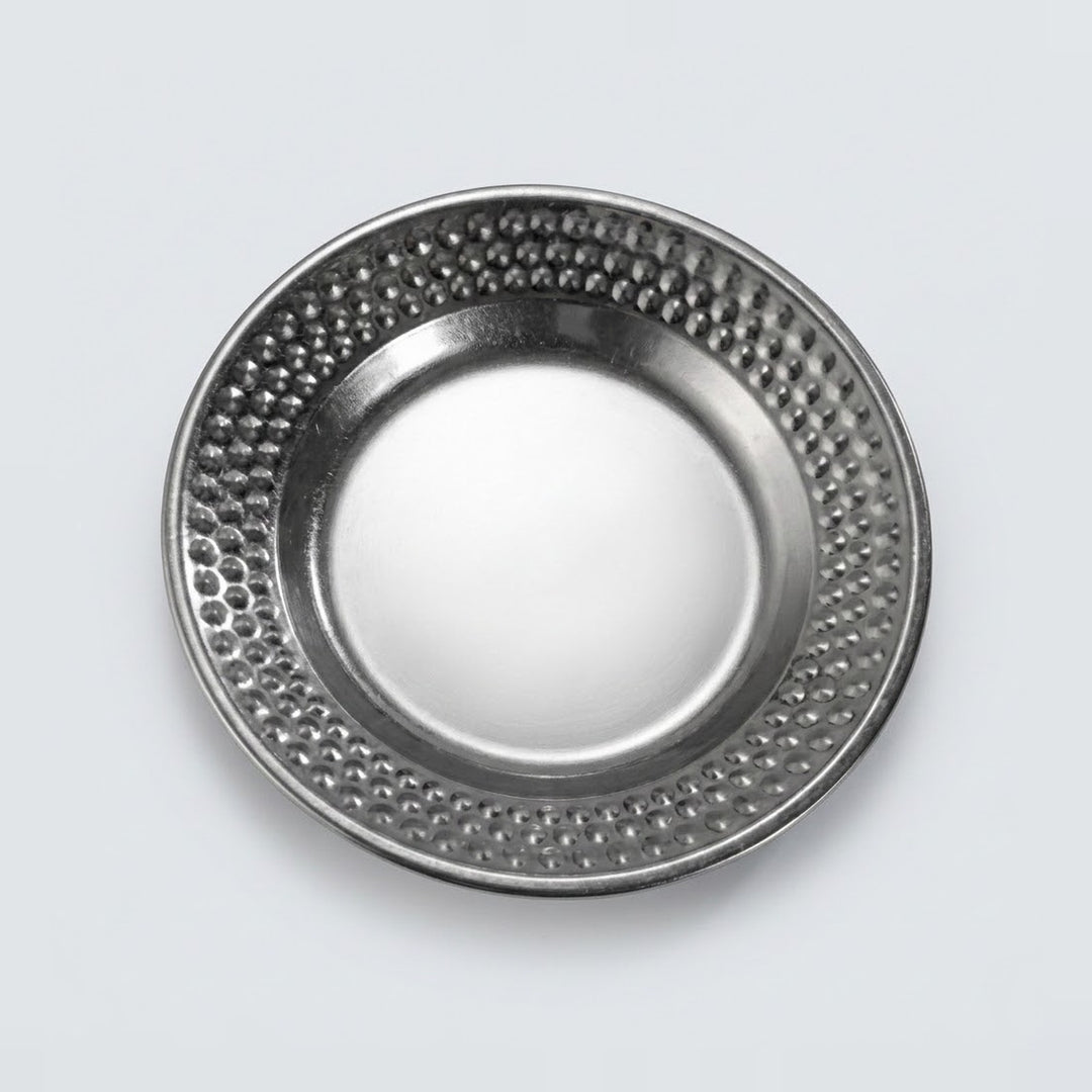 A round metallic silver plate with a textured, dimpled pattern around the rim, shown from a top-down perspective on a light gray background.