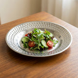 A hammered silver metal plate containing a fresh green salad with tomatoes and cucumbers, set on a wooden table.
