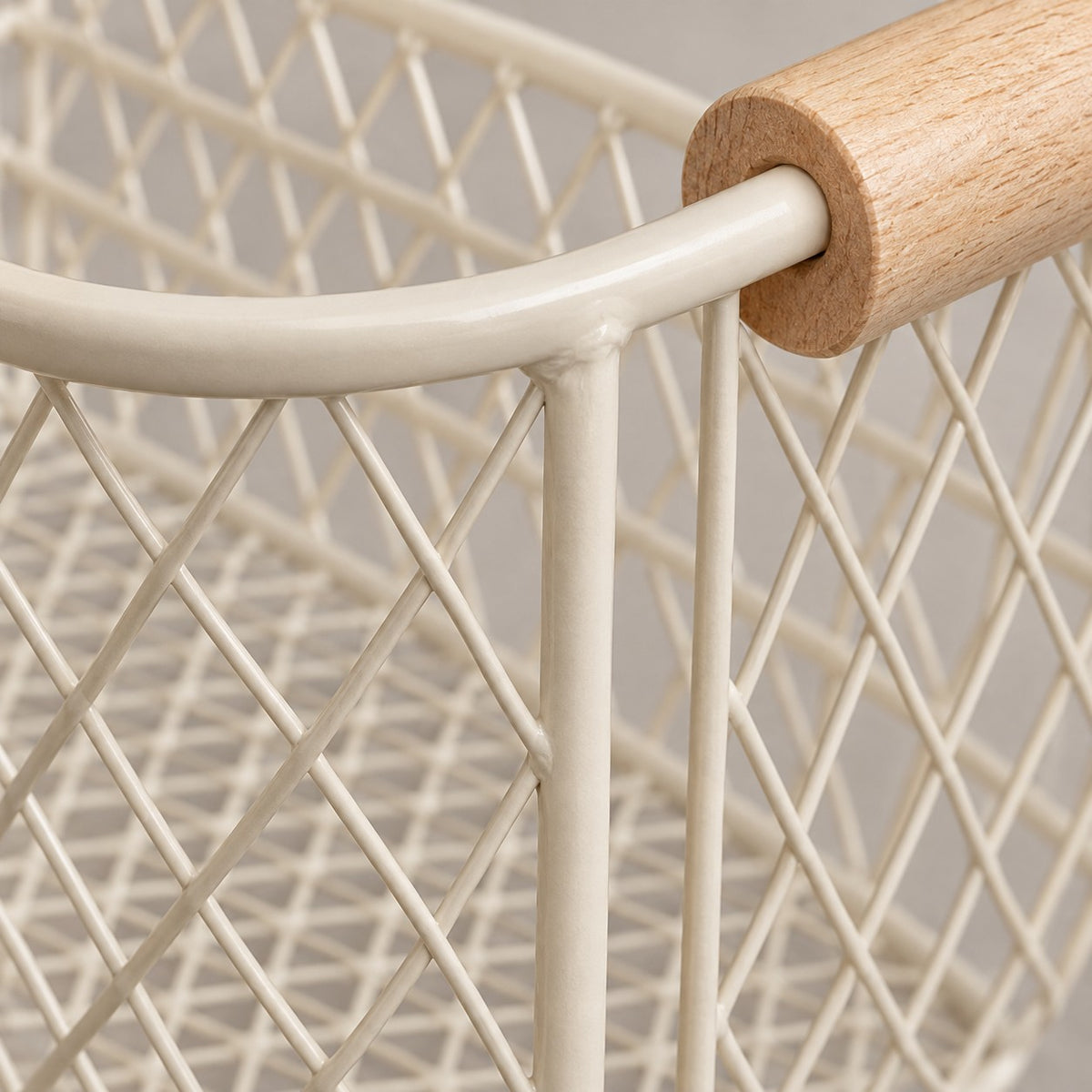 Close-up of the beige wire basket's coated metal mesh, welded joints, and wood grain.