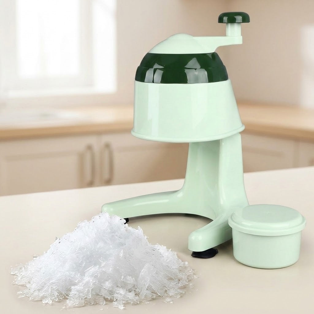 A mint green manual ice shaver with a dark green top section, shown on a kitchen counter with a pile of shredded ice and a small storage container.