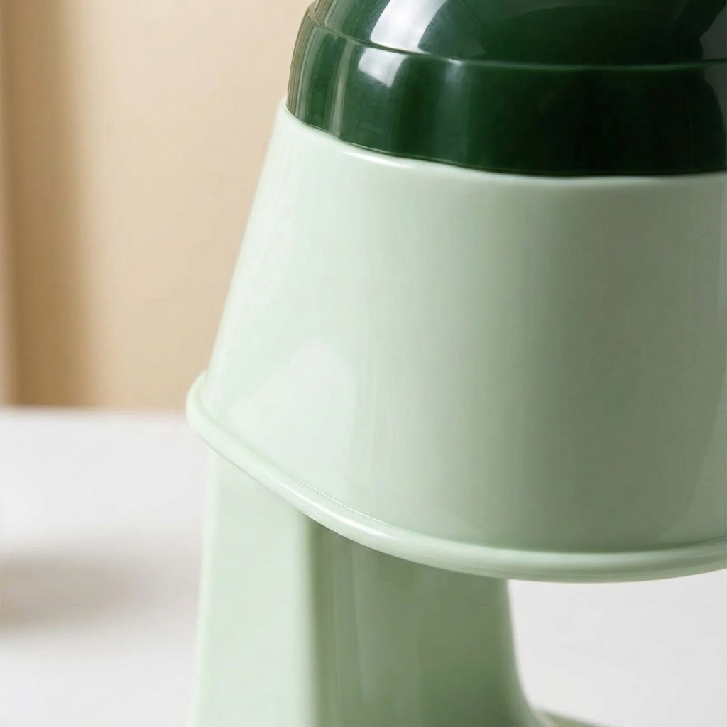 Close-up of a ceramic kitchen utensil, showing a glossy pale mint green body and a dark green top rim, set against a softly blurred beige background.