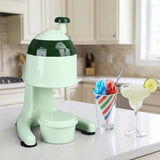 A mint green and dark green countertop ice shaker machine sits on a white kitchen counter next to a striped cup of colorful shaved ice and a margarita glass.