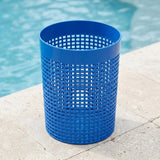 A bright blue plastic mesh trash can with a solid rim, placed on a light stone deck next to a swimming pool.