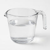 A clear glass measuring pitcher with a handle and pouring spout, partially filled with water, shown on a light gray background.