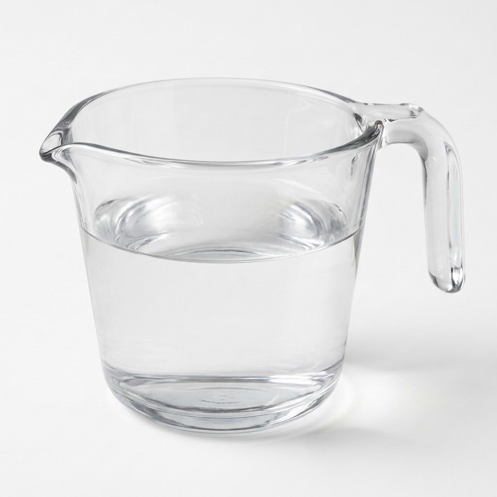 A clear glass measuring pitcher with a handle and pouring spout, partially filled with water, shown on a light gray background.