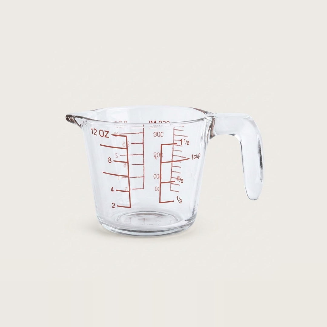 A clear glass measuring cup with red measurement markings and a handle, shown on a plain light beige background.