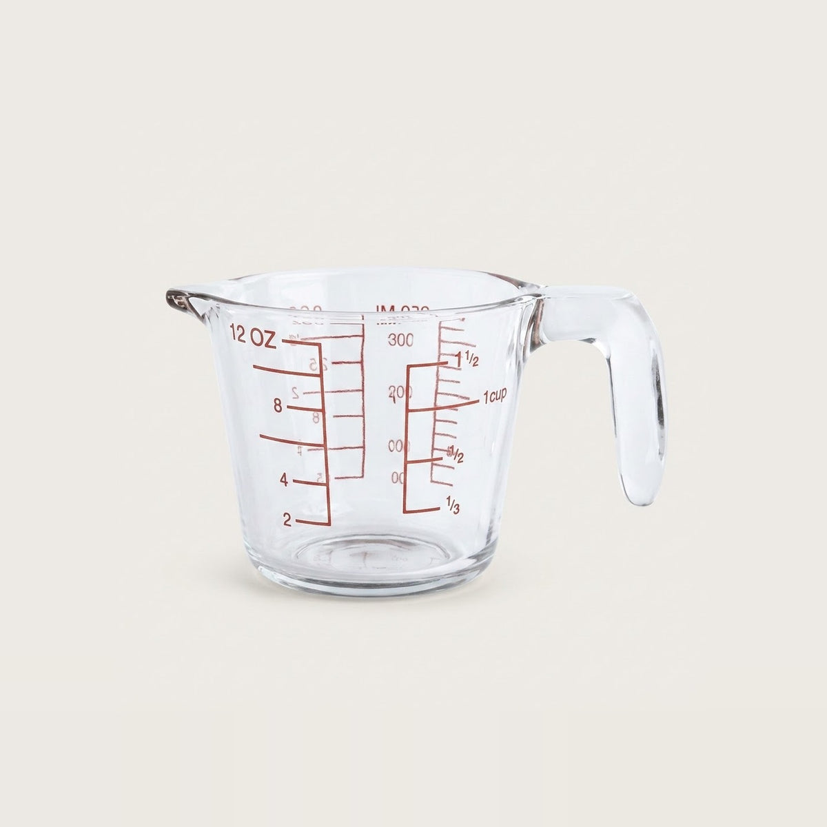 A clear glass measuring cup with red measurement markings and a handle, shown on a plain light beige background.