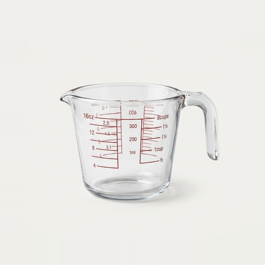 Clear glass measuring cup with red measurement markings and a curved handle, shown on a plain light background.