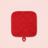 A square red bath mat with rounded corners and a small hanging loop, shown on a solid pale pink background.