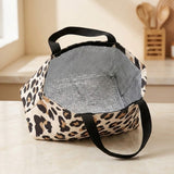 A leopard print insulated lunch bag with black handles, sitting on a light-colored countertop in a kitchen setting.