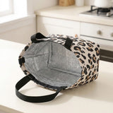 A leopard print insulated lunch bag with black handles, shown open on a kitchen counter with a silver foil lining.