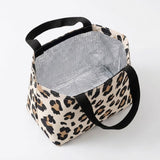 A leopard print canvas lunch bag with black handles and a silver reflective inner lining, shown on a plain white background.