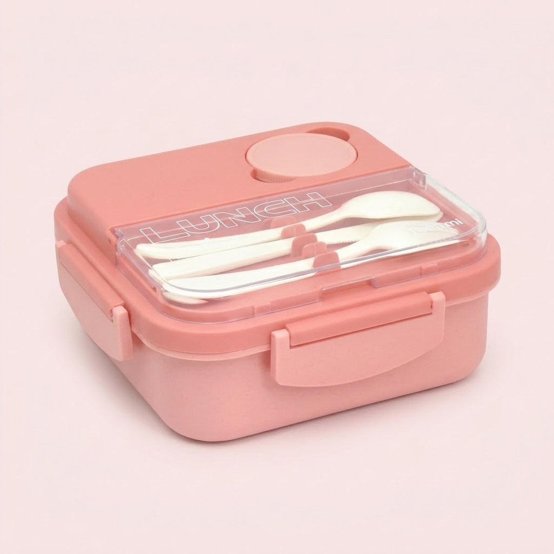 A pink plastic lunch box with a clear lid, containing white utensils, set against a solid pale pink background.